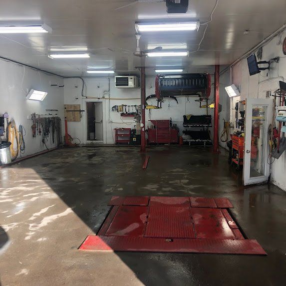 À l'intérieur d'un atelier de réparation automobile blanc, avec un pont élévateur rouge, des outils et un éclairage puissant au plafond.
