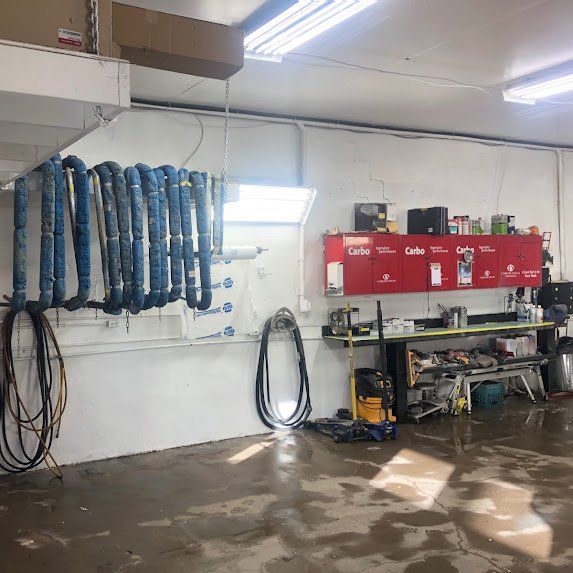 Mur d'atelier avec tuyaux d'arrosage bleus suspendus, armoires rouges et outils sur une étagère.