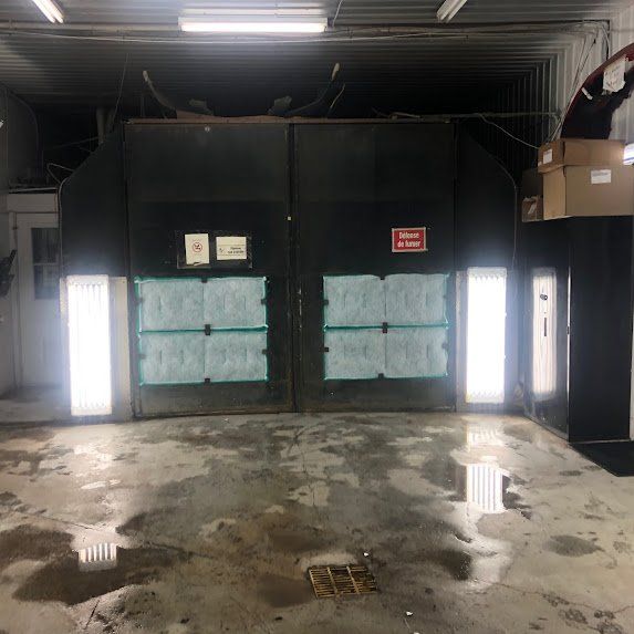 Garage industriel humide avec double porte noire fermée et éclairage latéral puissant.