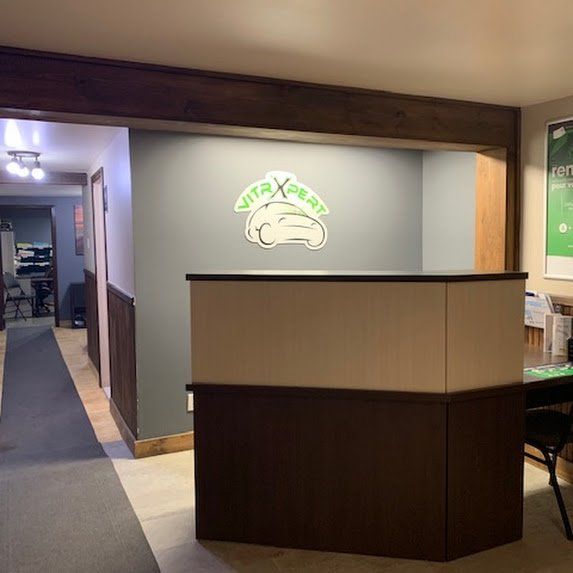 Bureau d'accueil vide avec façade en bois foncé et logo mural gris derrière.