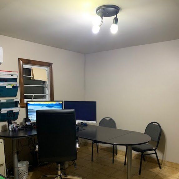 Petit bureau avec un bureau, des écrans d'ordinateur, des chaises et une table ronde sous des lampes au plafond.