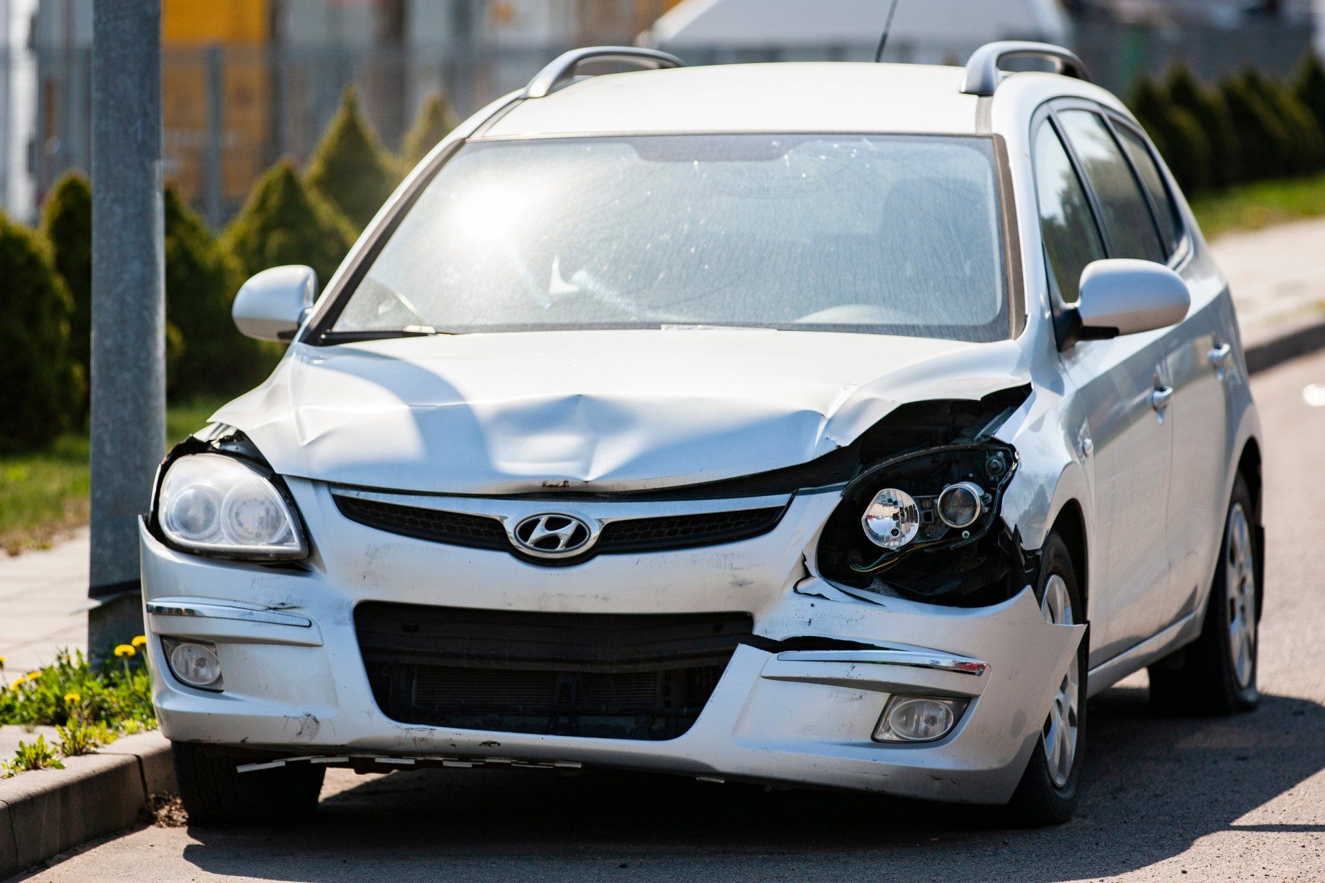 Une berline Hyundai blanche endommagée, avec un pare-chocs avant enfoncé, est garée dans la rue.