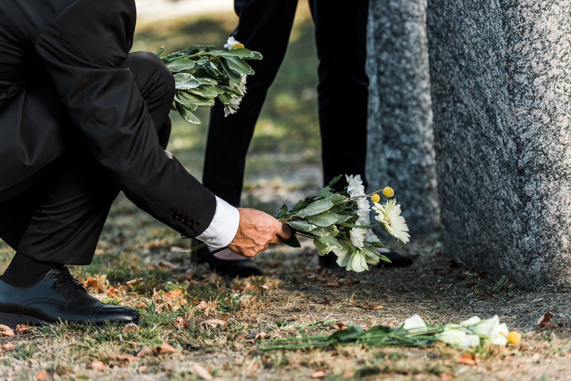 Una persona si inginocchia per deporre fiori bianchi su una lapide in un cimitero.