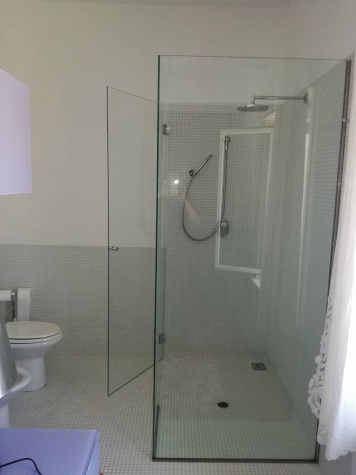 Box doccia in vetro in un bagno con piastrelle bianche e WC.