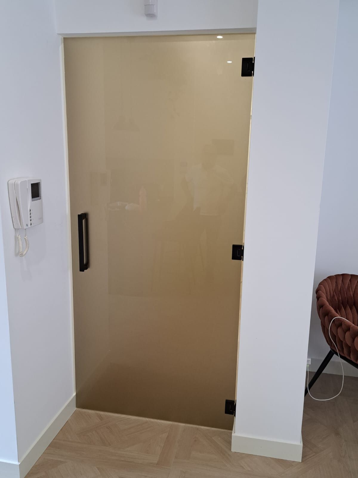 Porta in vetro smerigliato con ferramenta nera, inserita in una parete bianca.