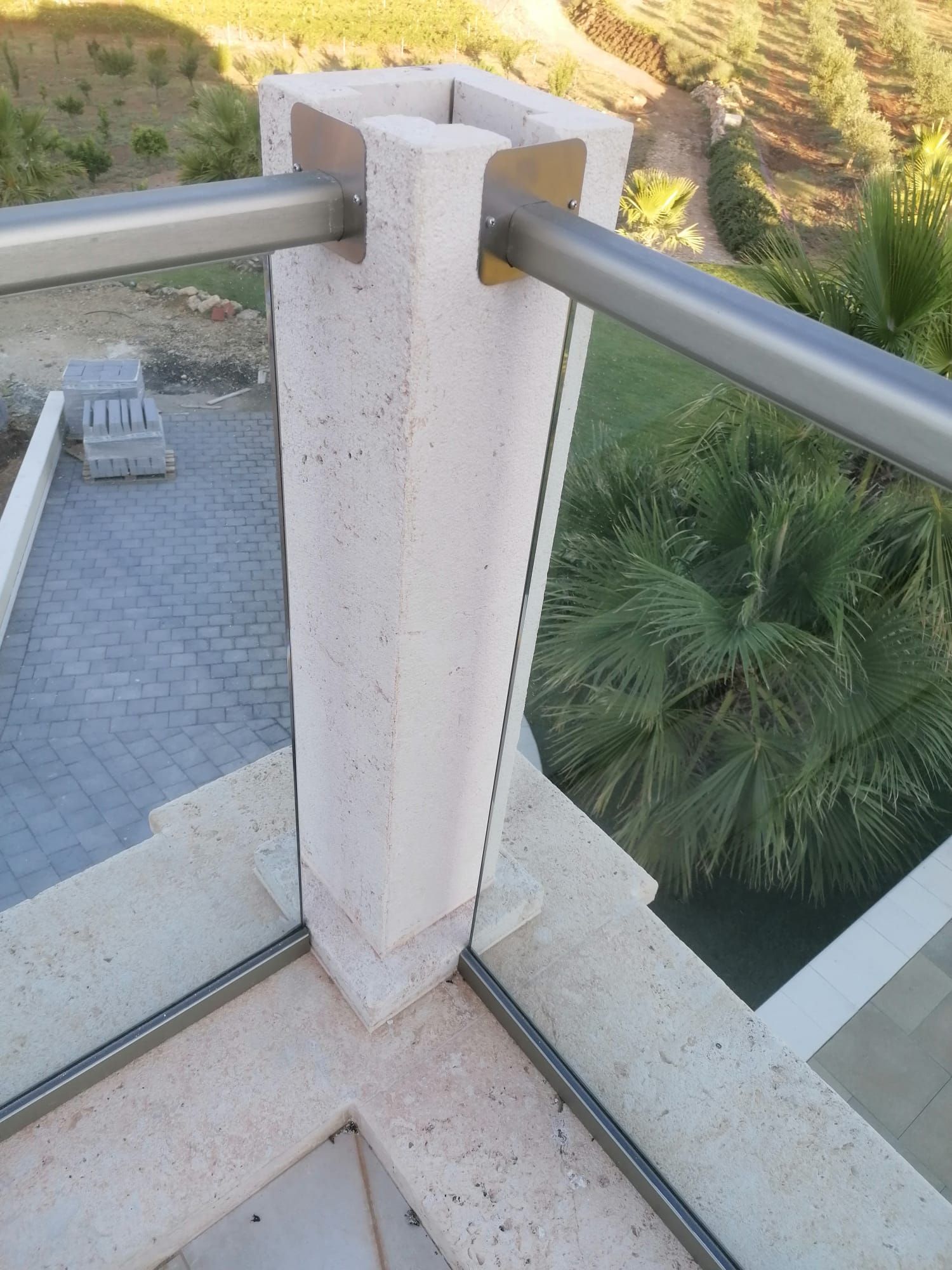 Ringhiera in cemento e acciaio con pannelli in vetro su una terrazza esterna con vista sul verde.