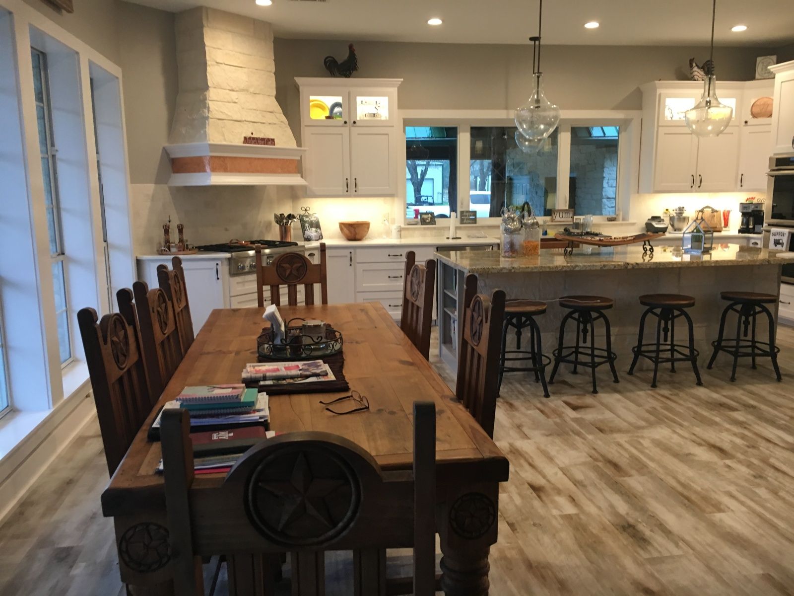 Kitchen with dining table, island, white cabinets, stone range hood, and wood floors.
