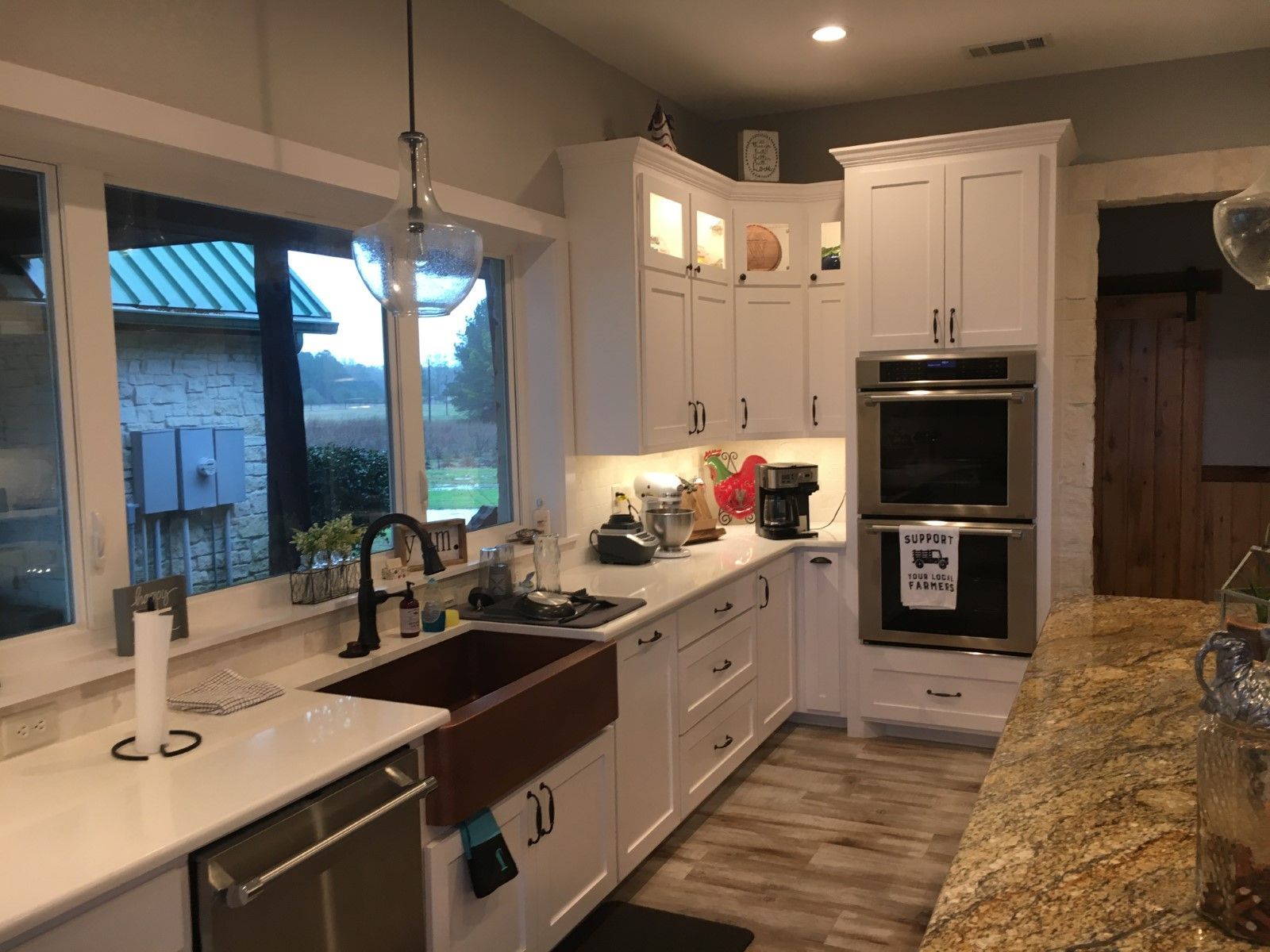 White kitchen with copper sink, double oven, and a view through a window.