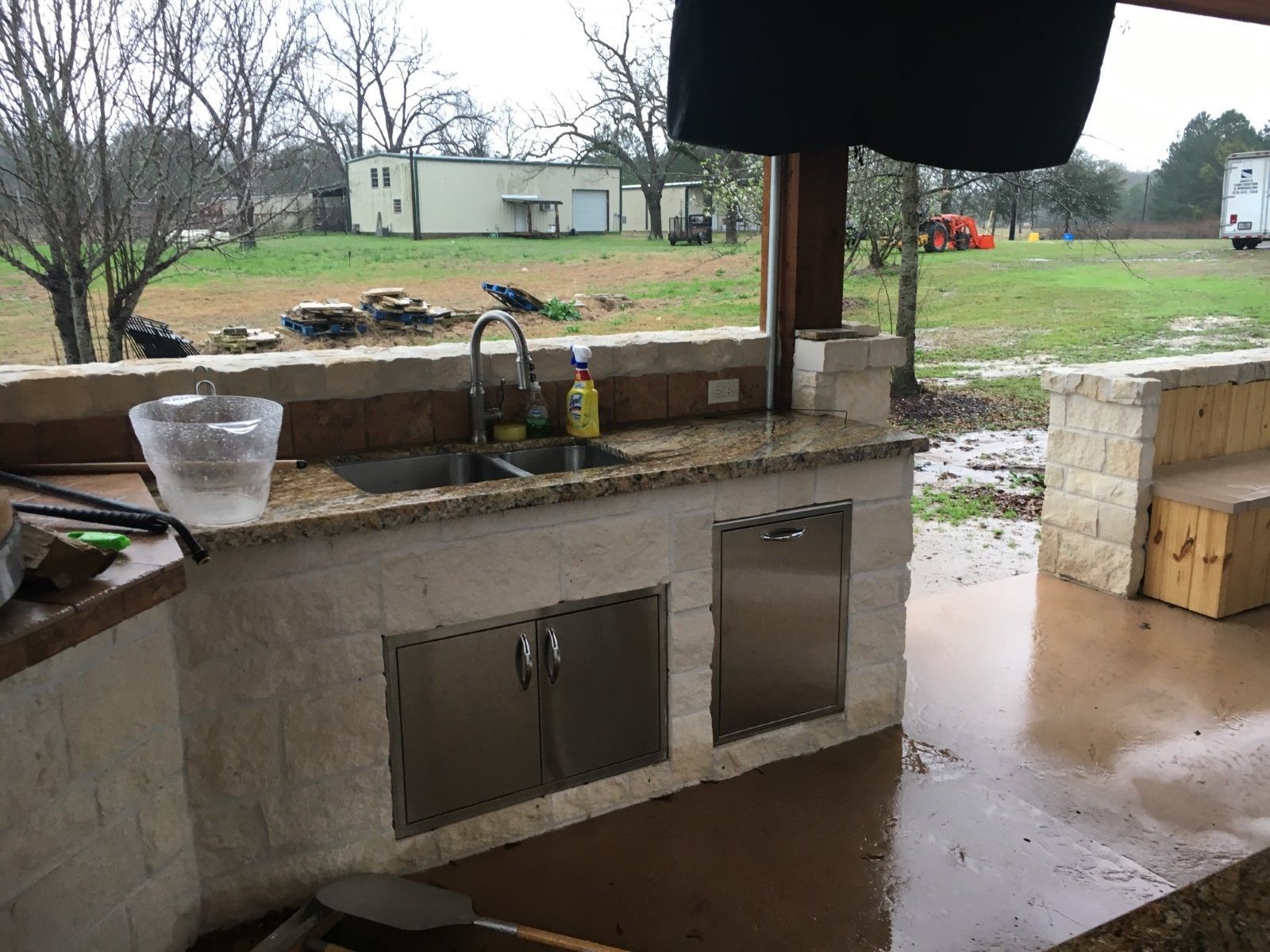 Outdoor kitchen with granite countertop, stainless steel appliances, and sink, in a covered patio setting.