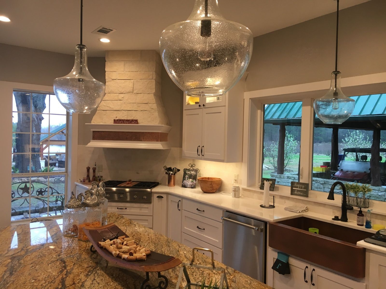 Kitchen with granite countertops, white cabinets, copper sink, pendant lights, and window views.