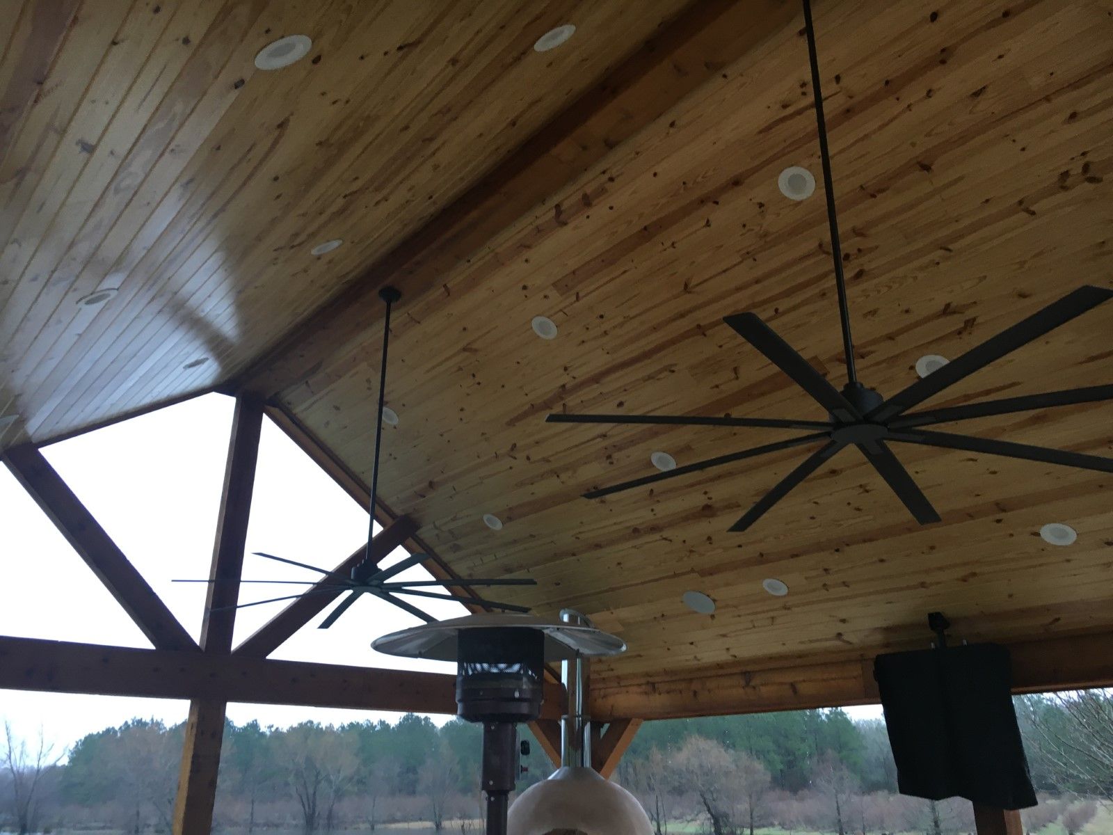 Wooden ceiling with recessed lights, two large fans, and a patio heater.