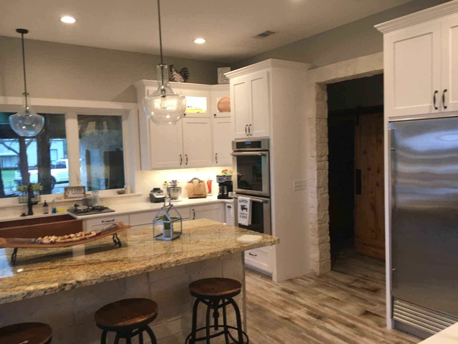 Spacious kitchen with white cabinets, granite island, stainless steel appliances, and wooden floors.