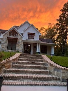 Brick stairs lead to a white house with a stone facade, sunset sky overhead.