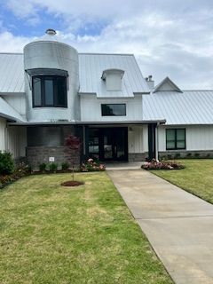 White modern building with silo, black windows and door, walkway, green lawn.