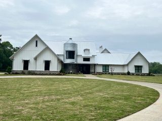 White farmhouse with gray stone accents and metal roof, driveway, and overcast sky.
