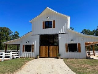 White barn with wooden doors and accents, gravel driveway, blue sky.