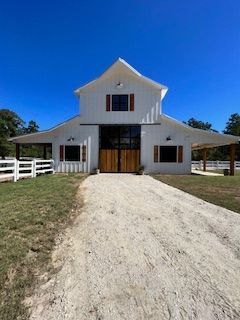 White barn with wooden doors, a gravel driveway, and a clear blue sky.