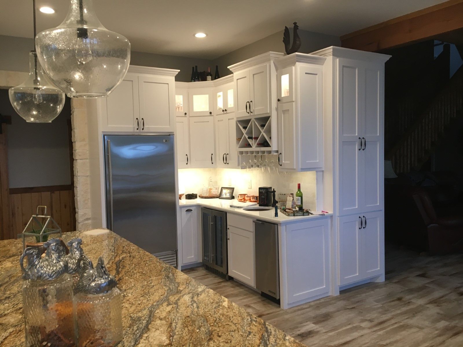 White kitchen cabinets surround a stainless steel refrigerator and appliances. Granite countertop in foreground.