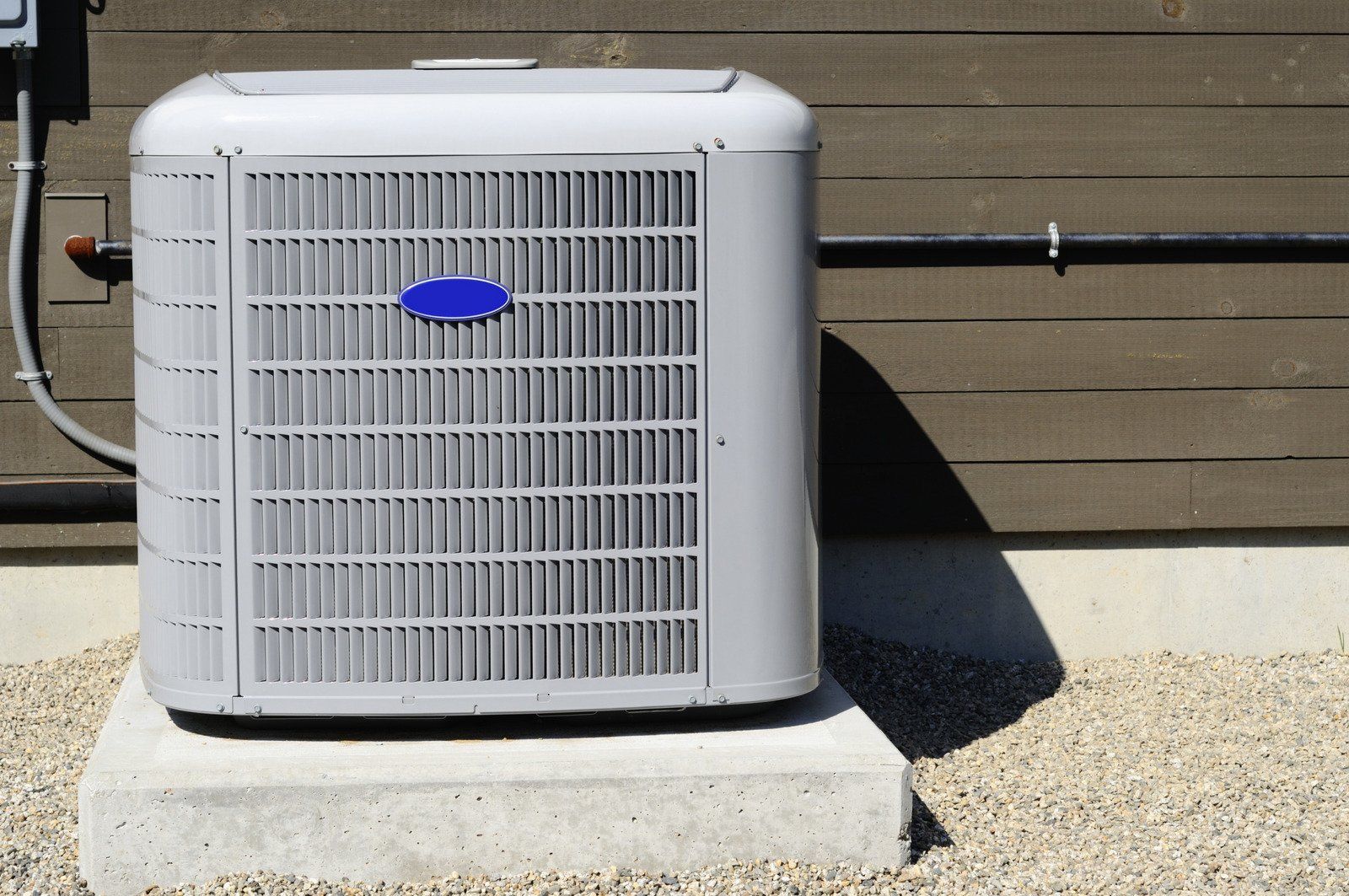 White outdoor air conditioner unit beside a house wall on a concrete pad and gravel.