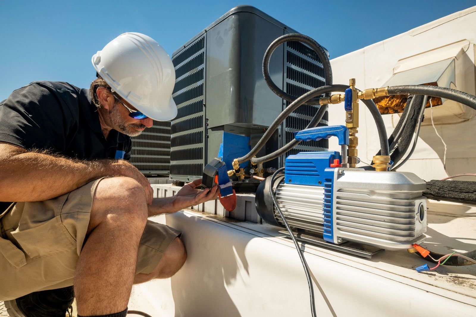 Worker in hard hat inspecting rooftop HVAC equipment beside a large cooling unit