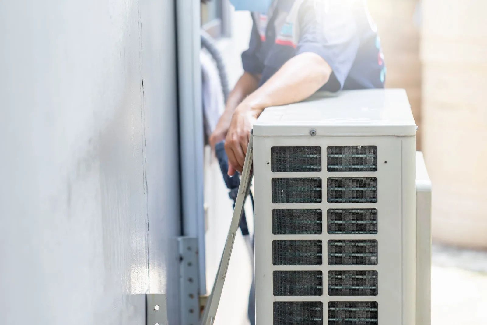 HVAC technician installs an air conditioning unit outside a building, wearing a mask.