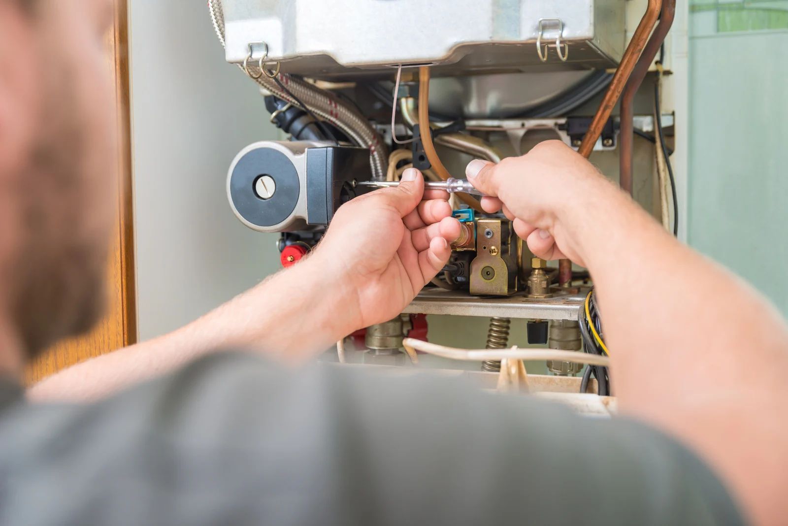 Technician adjusting wiring inside an open boiler unit