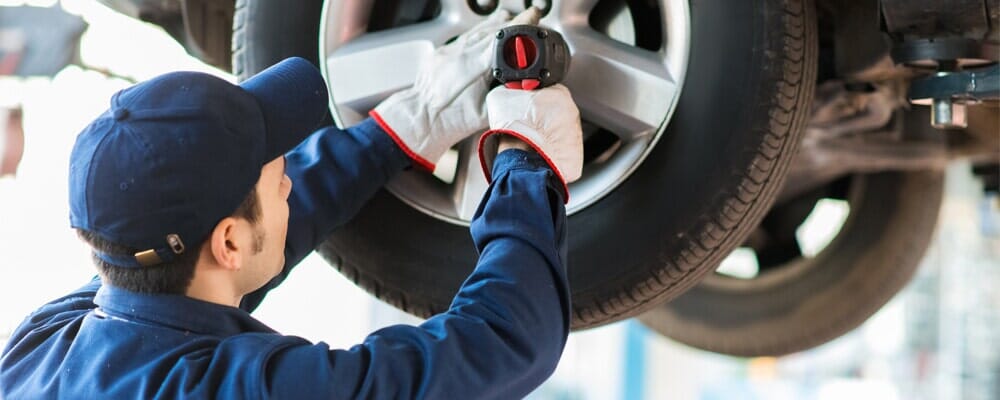 A man is changing a tire on a car in a garage.