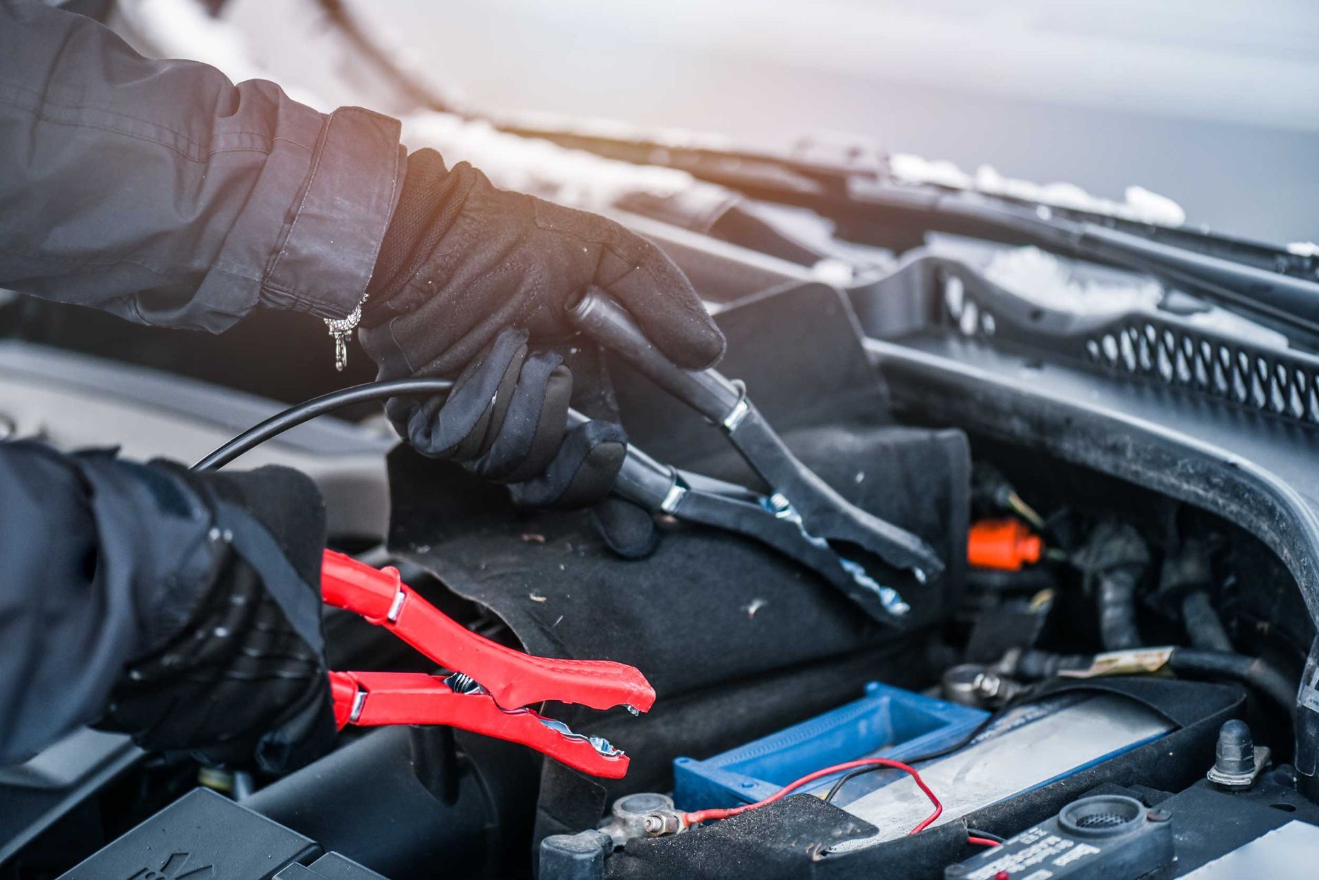 A pair of hands charge a car battery with electricity trough electric cables.