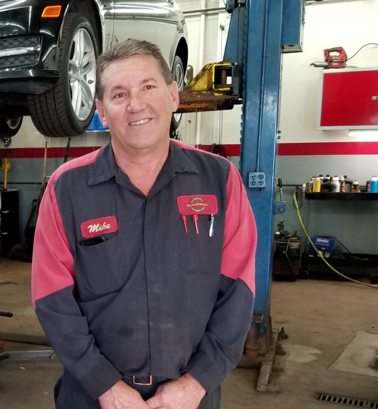 Three mechanics are standing in front of a car on a lift in a garage.
