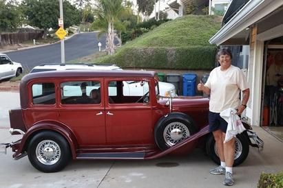 A man is standing in front of a red car giving a thumbs up