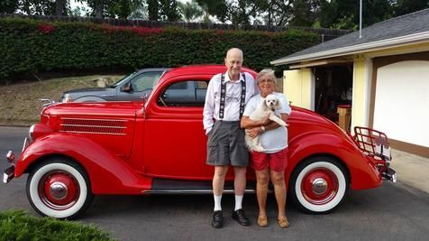 A man and woman are standing in front of a red car.