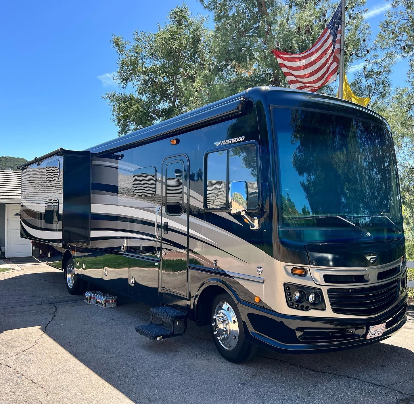 A large rv is parked in a driveway with an american flag on top of it.