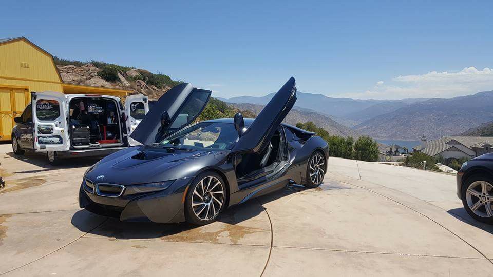 A bmw i8 is parked on a concrete driveway with its doors open.