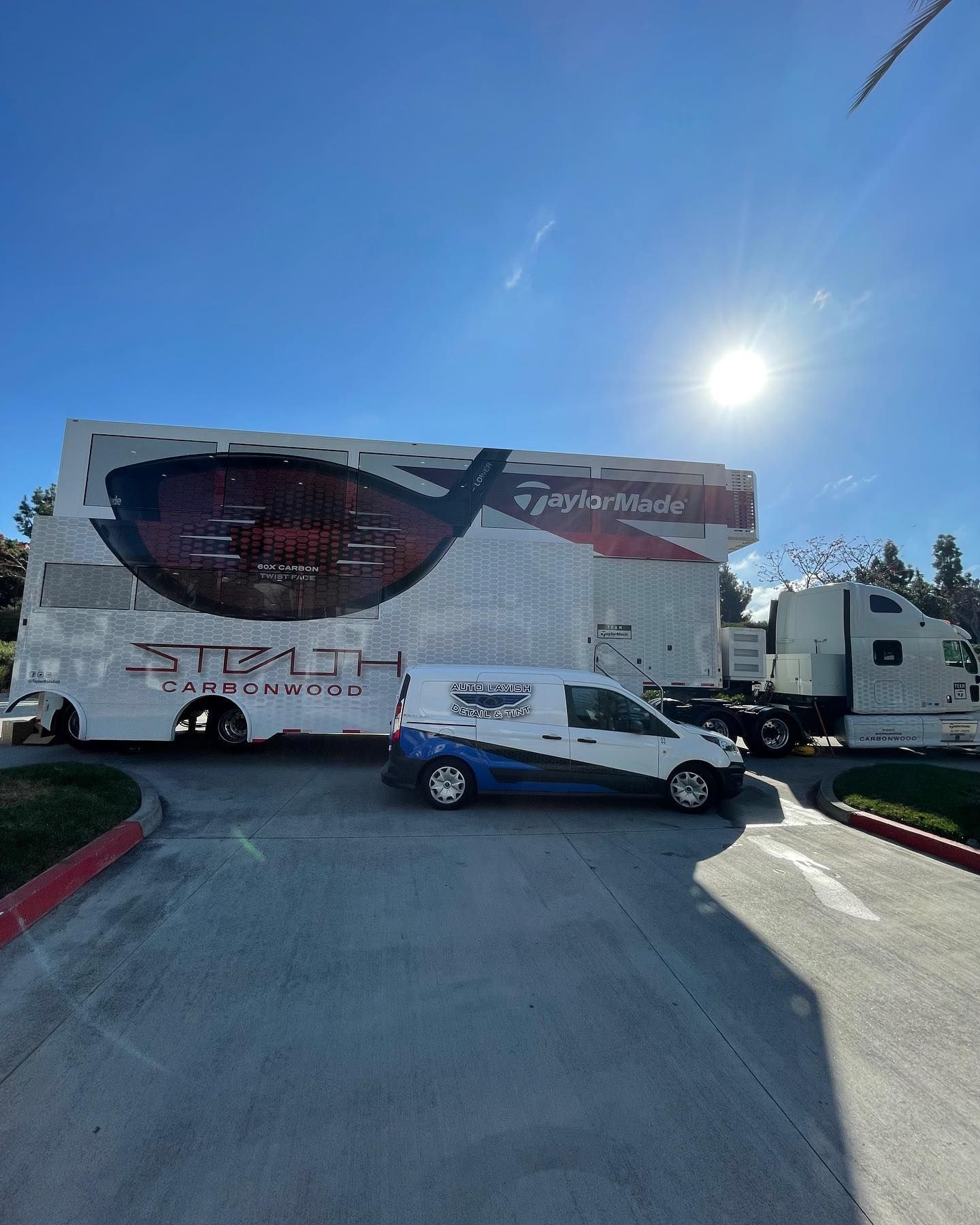 A white van is parked in front of a large trailer.