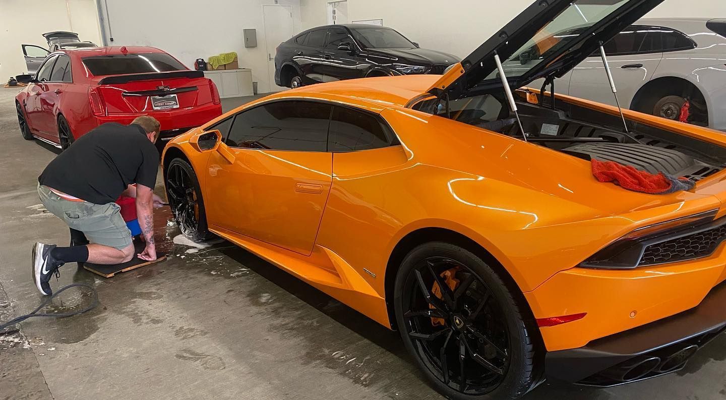 A man is kneeling down next to an orange sports car.