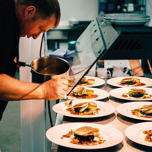 A man is preparing food on plates in a kitchen.