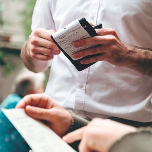 A man in a white shirt is holding a notepad and a pen