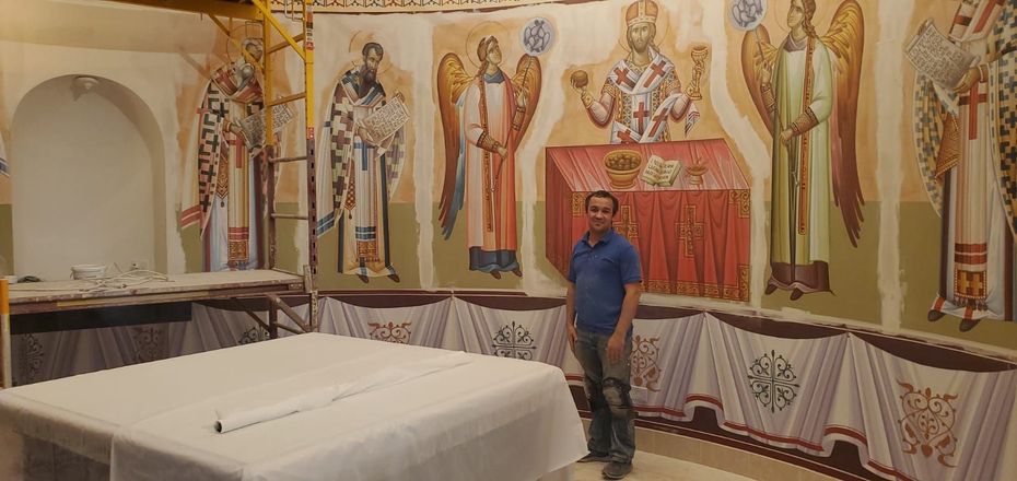 A man is standing in front of a painting on the wall of a church.