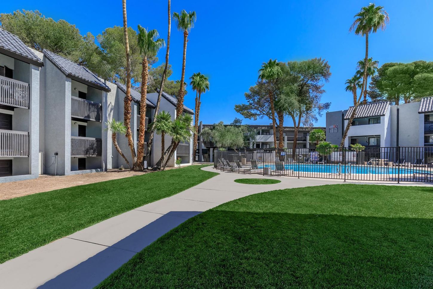 Apartment complex exterior with pool and palm trees under a clear blue sky.