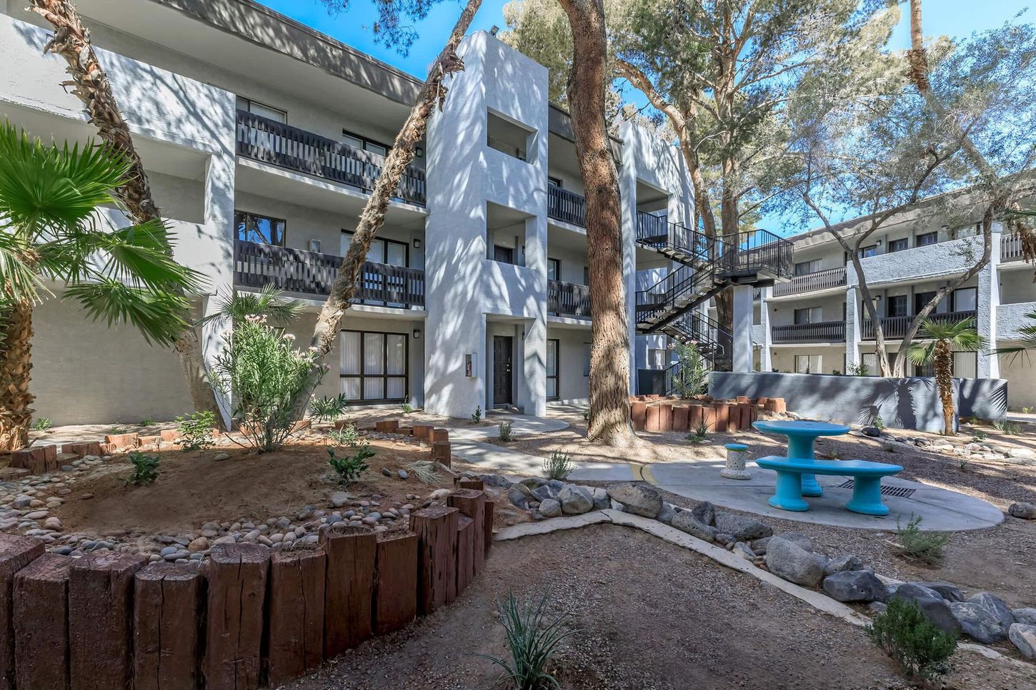 Courtyard of a multi-story apartment building with desert landscaping and a picnic table.