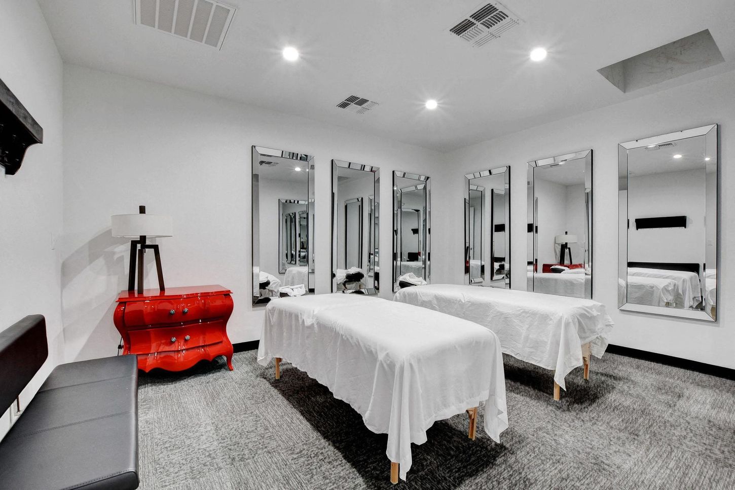 Massage room with two beds, large mirrors, red cabinet, and gray carpet.