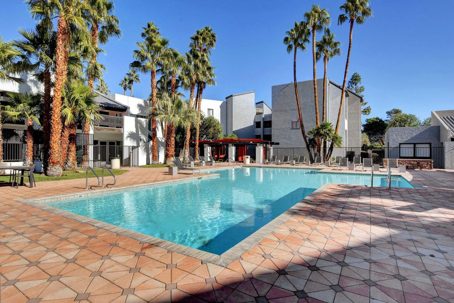 Pool and surrounding buildings with palm trees under a bright blue sky.