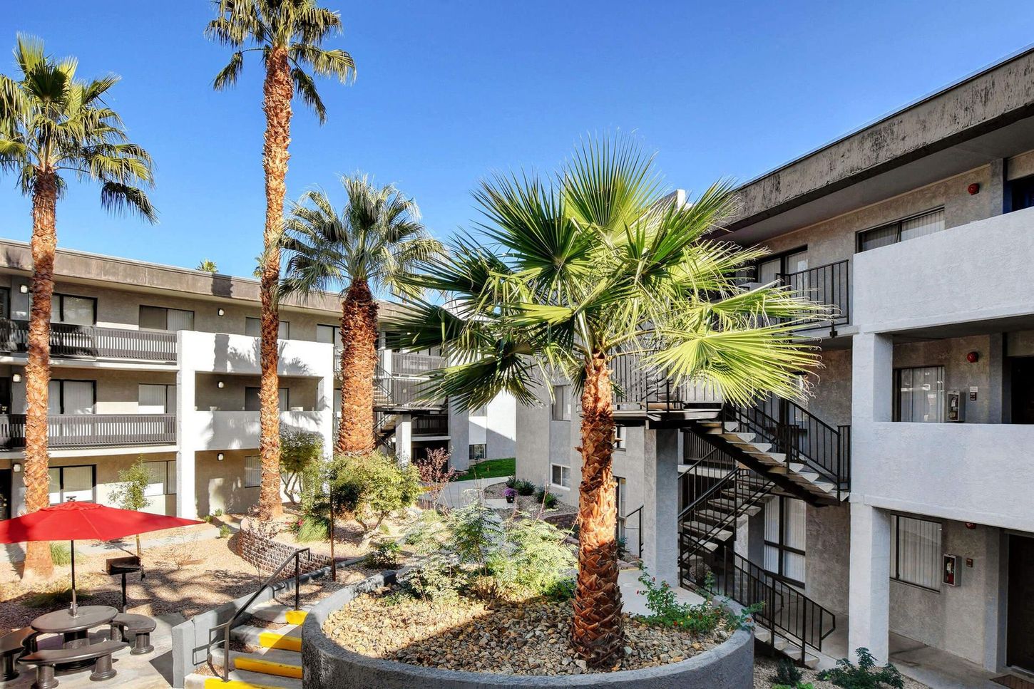 Courtyard apartment complex with palm trees, picnic tables, and exterior stairways.