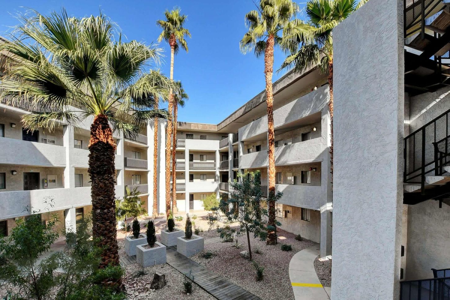 Courtyard apartment complex with palm trees and a blue sky.