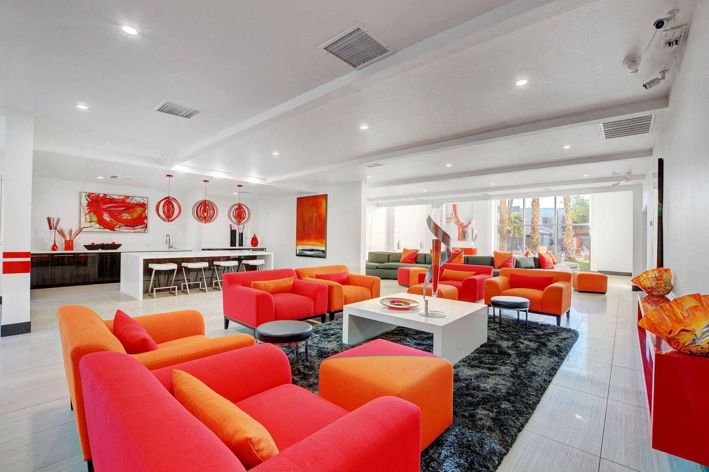 Modern living room with orange and red sofas, white walls, and a kitchen area.