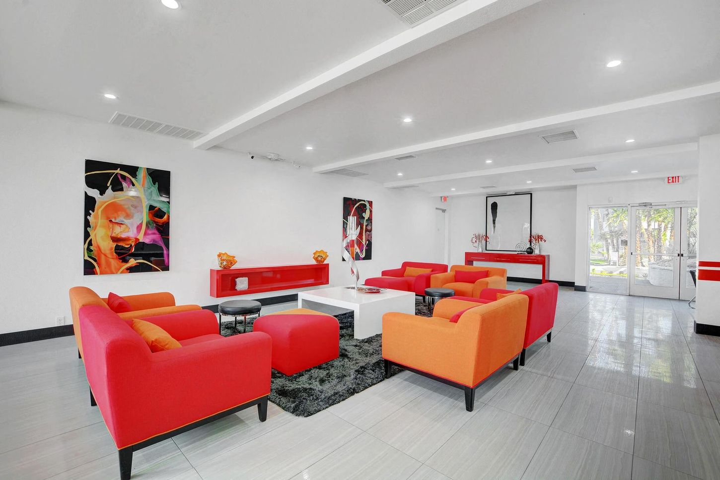 Modern lounge area with red and orange sofas, white walls, and colorful artwork.