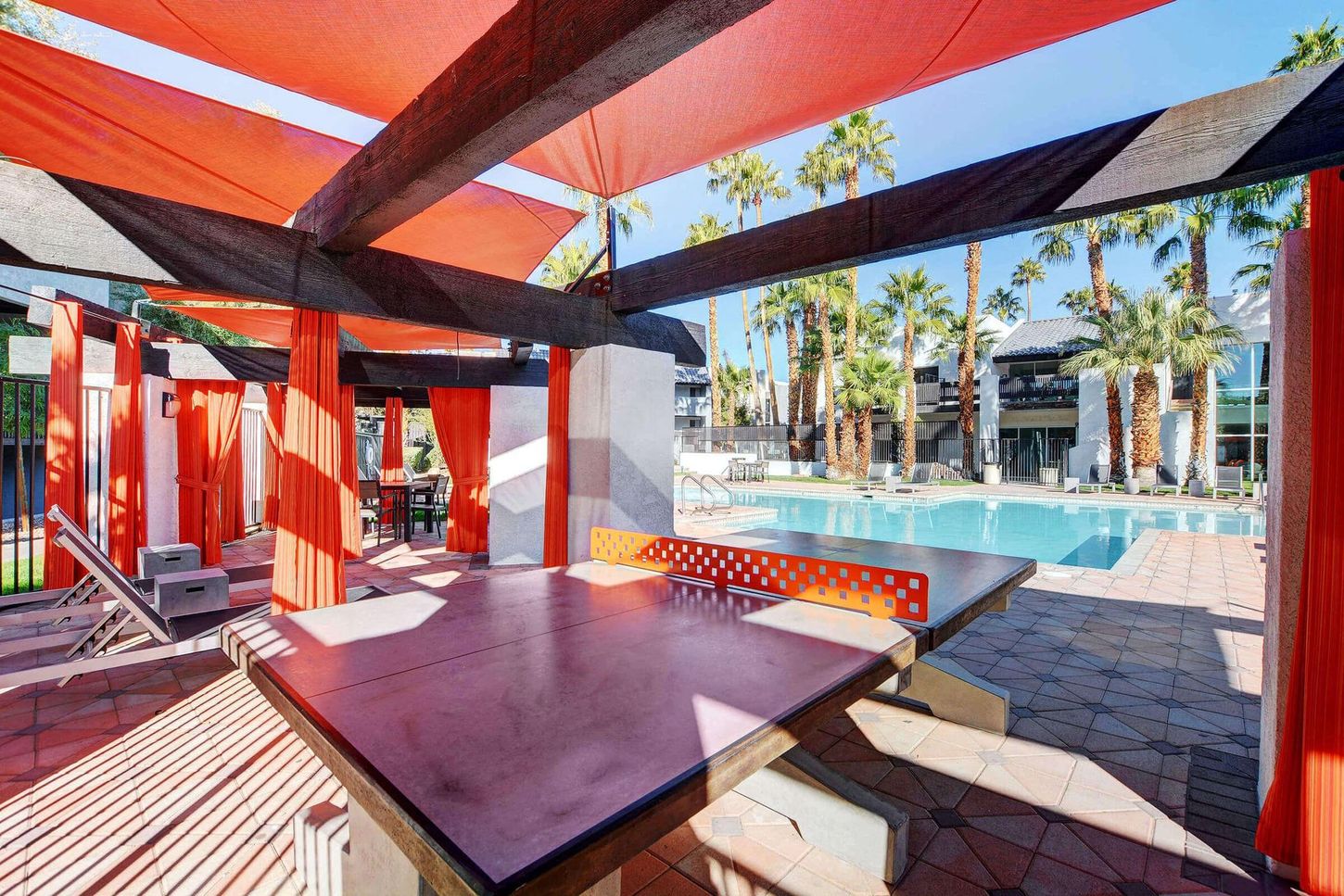 Outdoor patio with ping pong table, orange fabric, pool, and palm trees.