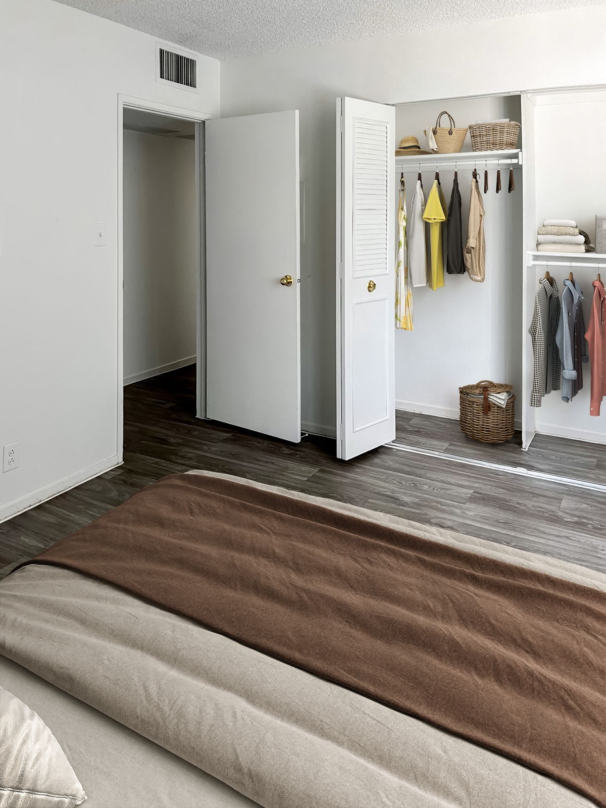 Bedroom with bed, open closet with clothes, and doorway to another room.