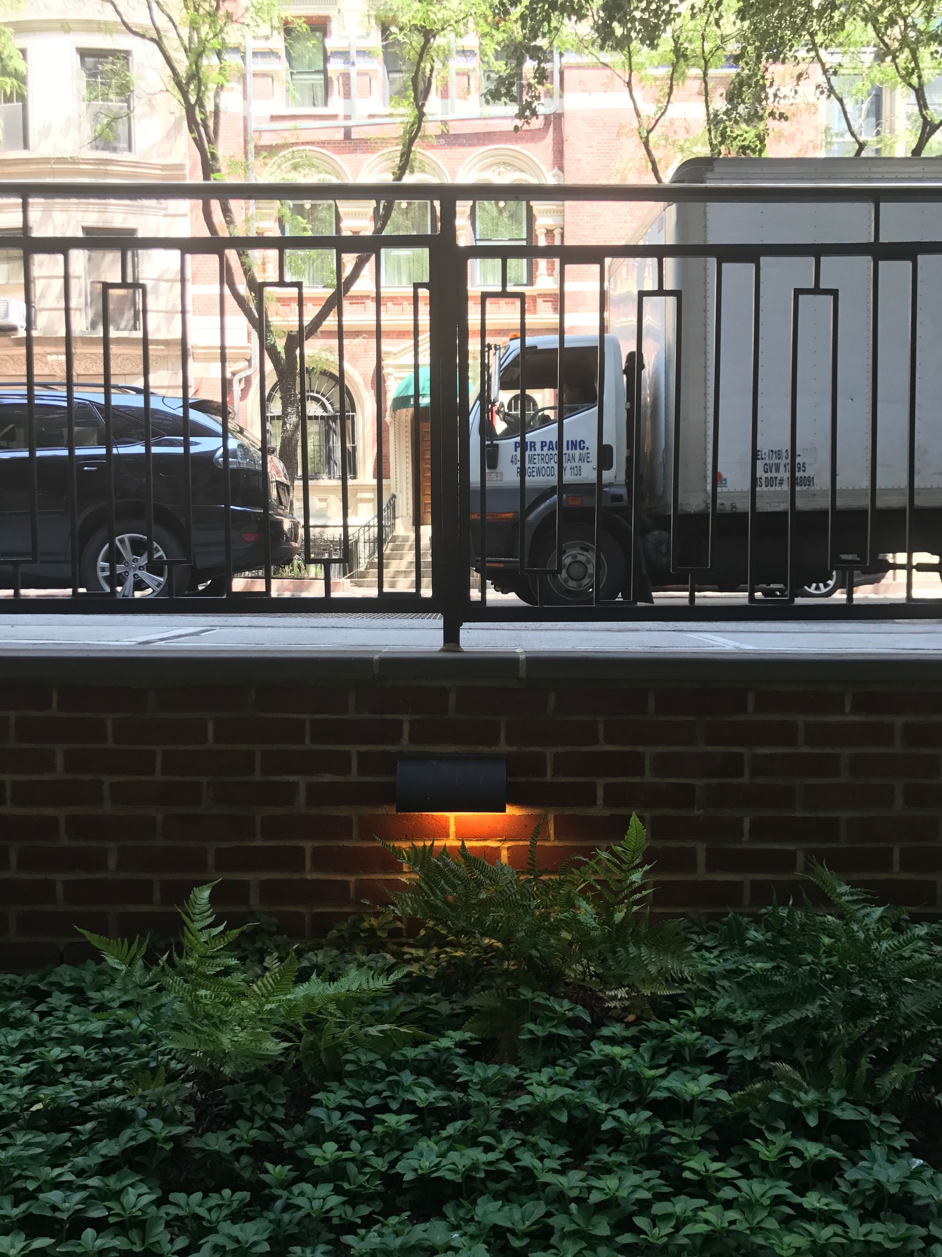 A white truck is parked behind a fence in front of a brick wall.