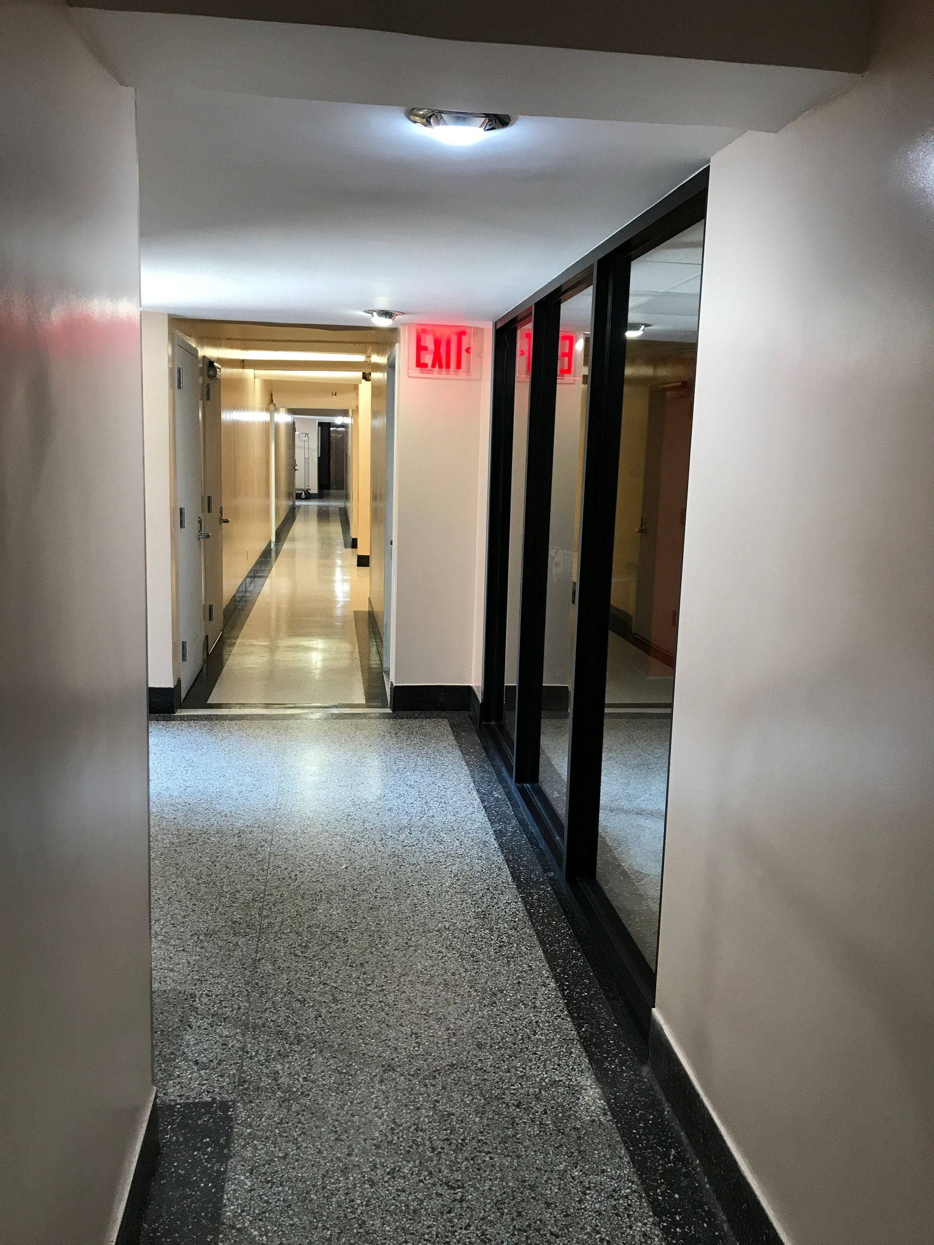 A long hallway with a red exit sign on the wall